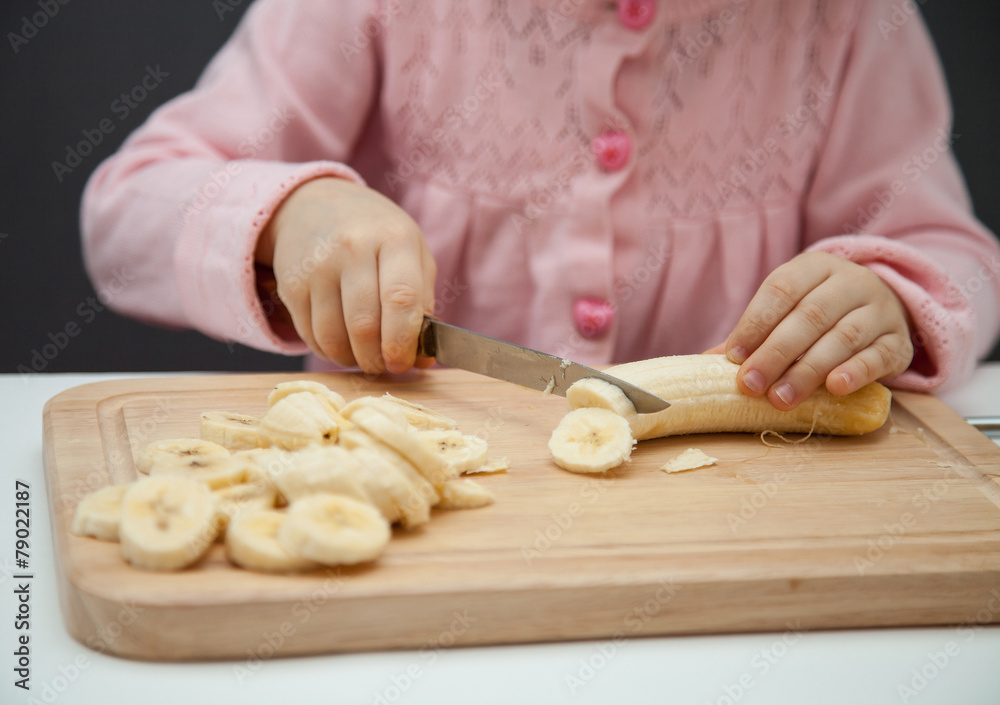 Little girl cutting a ripe banana