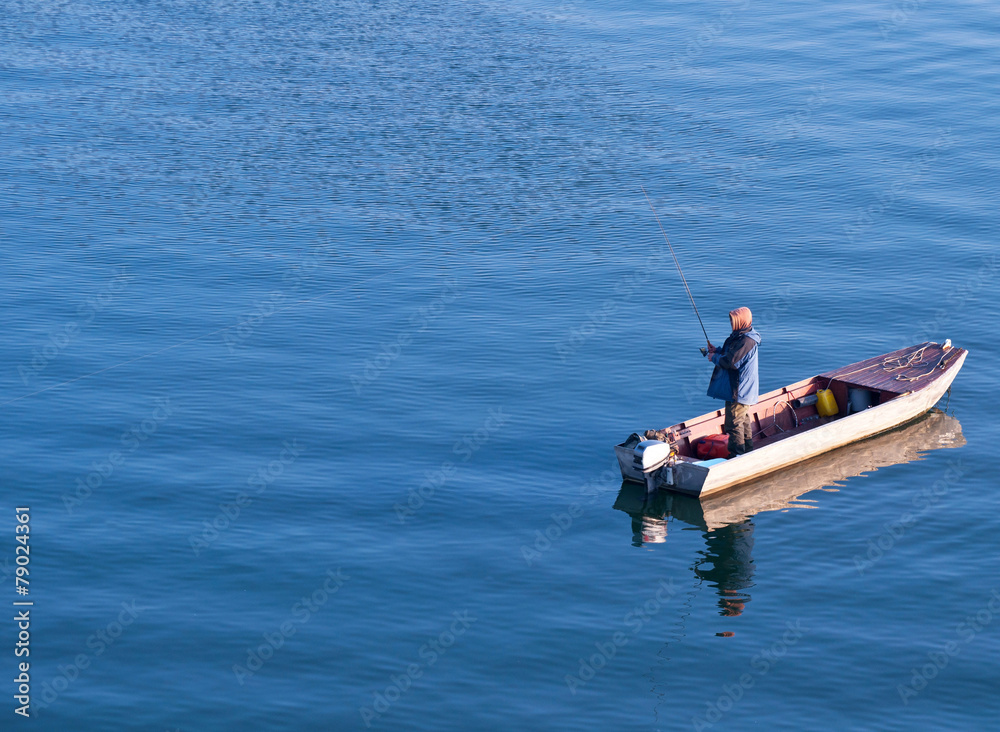 Fototapeta premium Fisherman standing on a boat and fishing in sea