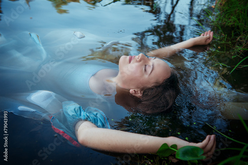 Young beautiful drowned woman in blue dress lying in the river