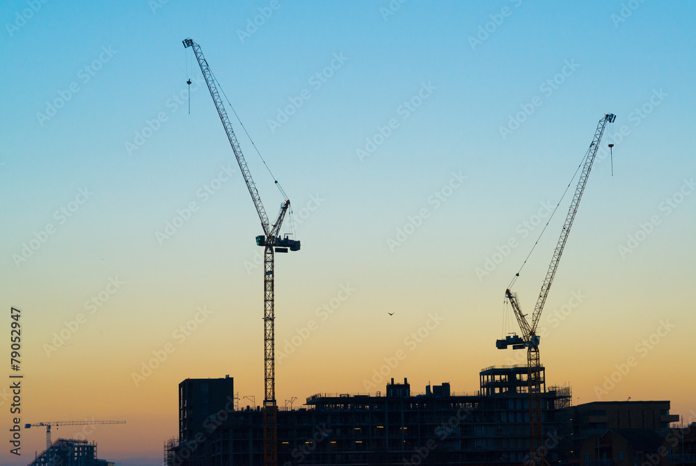 Silhouette of two massive construction cranes with sky at sunset