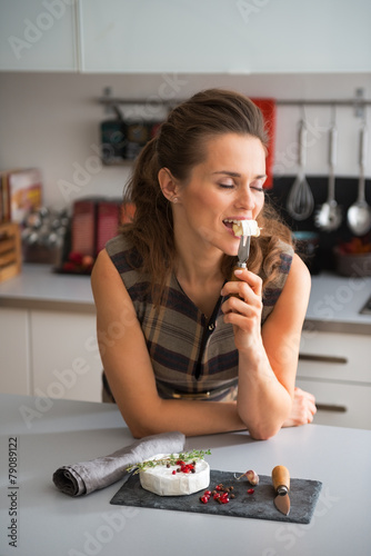 Young woman eating camembert in kitchen