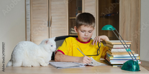 Happy boy doing homework with cat and books on table. Education