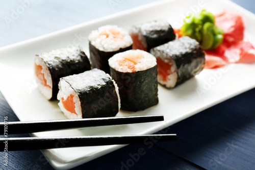 Sushi rolls with salmon on plate, on wooden background