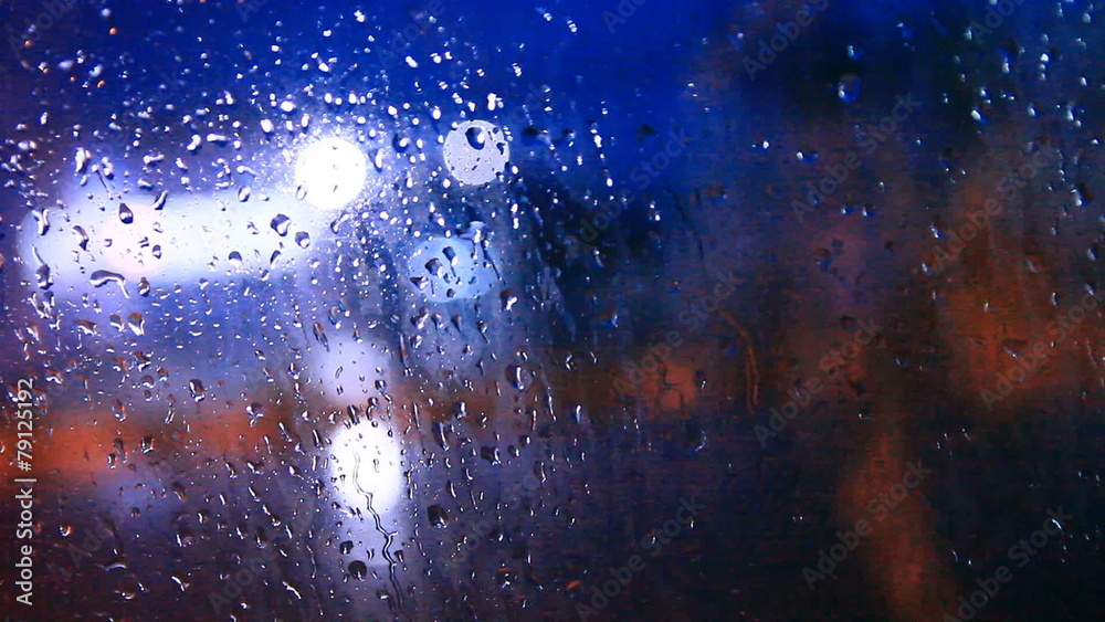 Rain drops and flows on front windshield of car, blurry light