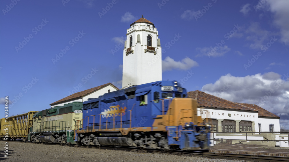 Train engine pulls its cars by the depot with blue sky