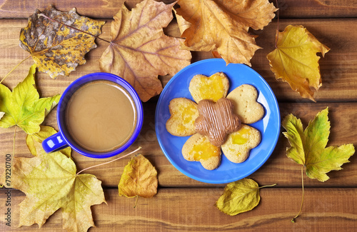 Cup of coffee and cookies on the table with dried autumn leaves.
