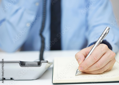 Businessman is talking on the phone and writing memo