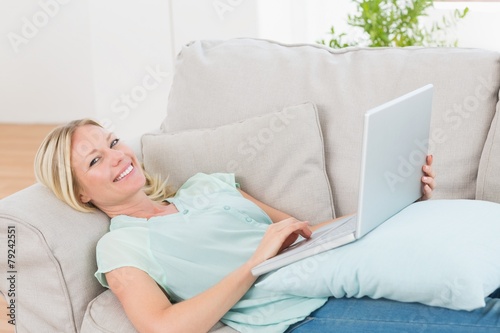Beautiful woman using laptop while lying on sofa
