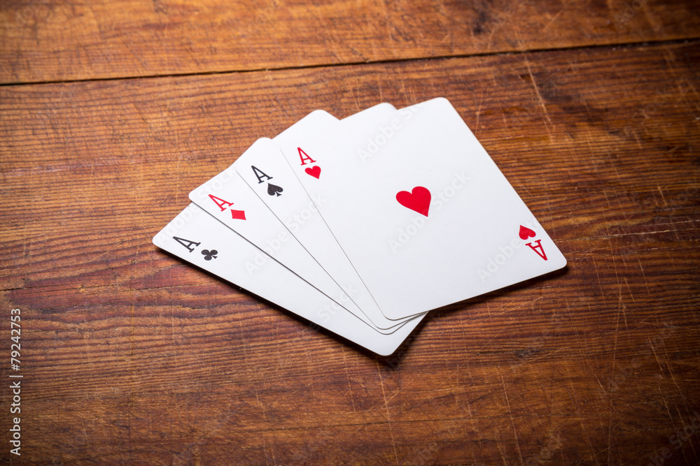 Obraz premium A group of four playing card aces on a stained oak wooden table.