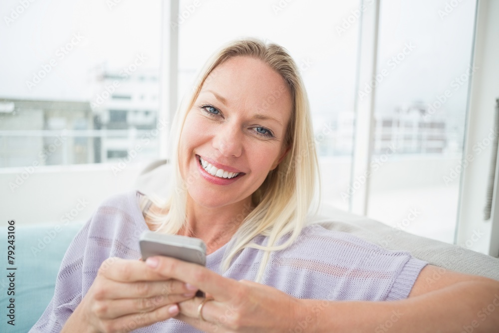 Smiling woman text messaging through mobile phone in living room Smiling woman text messaging through mobile phone in living room