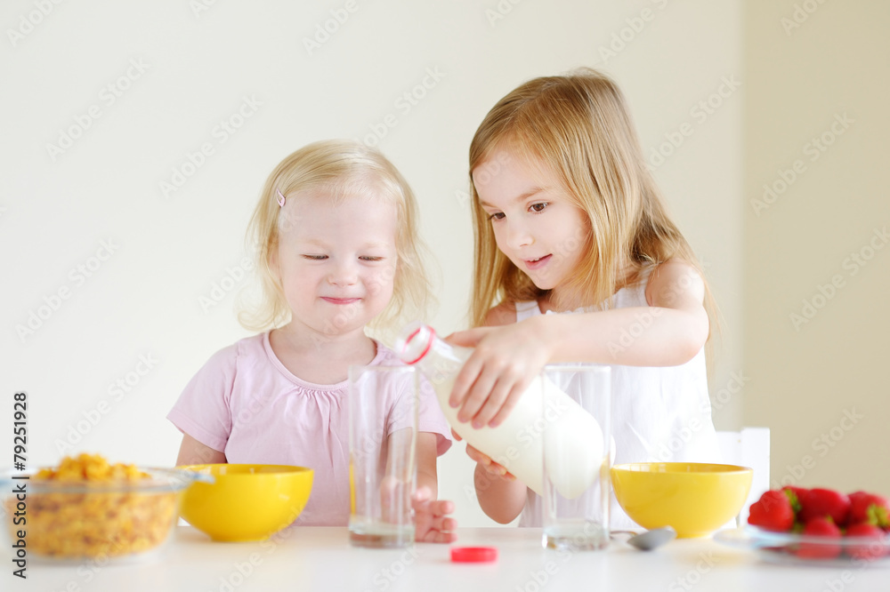Two cute little sisters eating cereal in a kitchen Two cute little sisters eating cereal in a kitchen