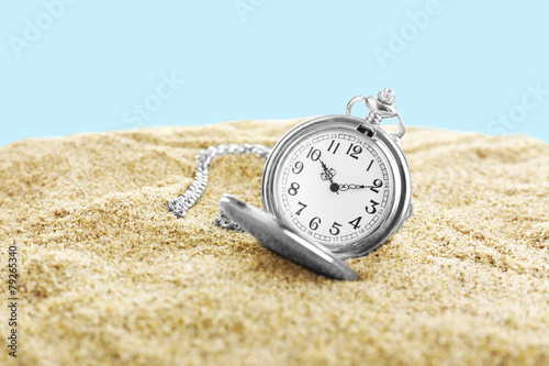 Silver pocket clock on sand on blue background