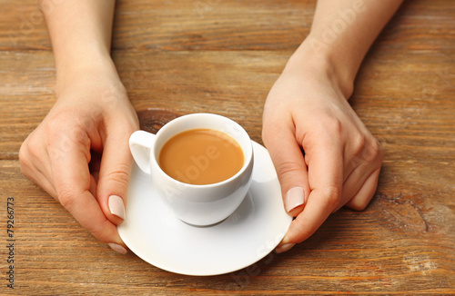 Female hands holding cup of coffee on wooden planks background