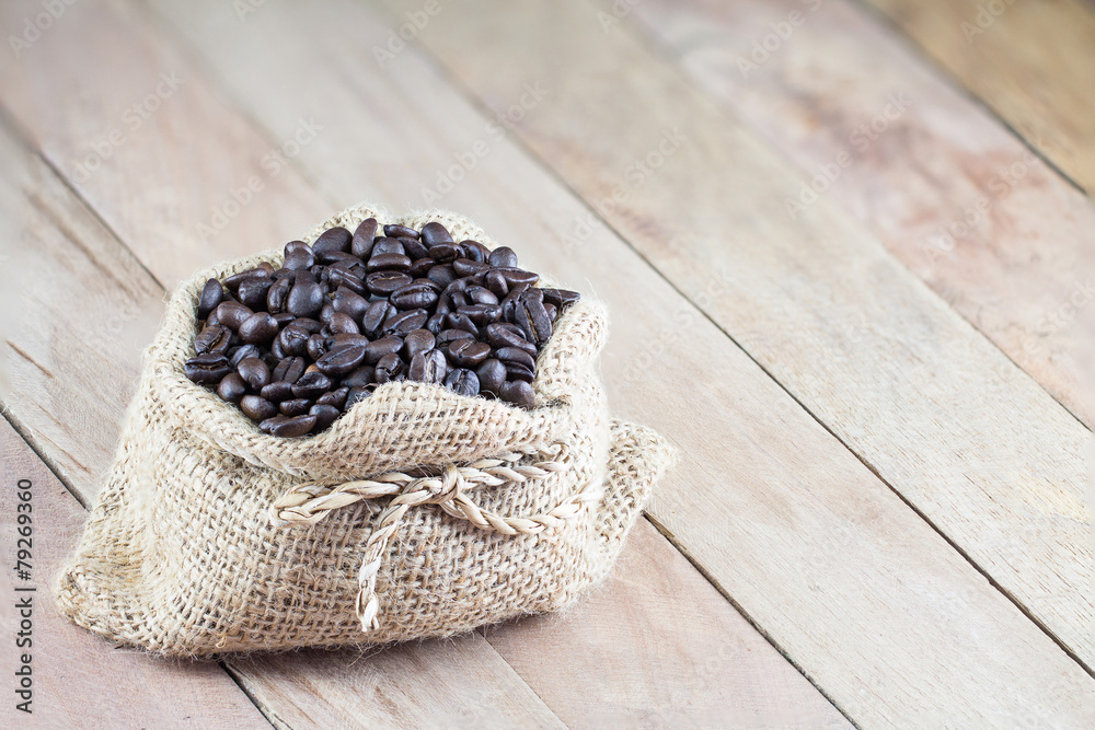 Coffee beans in coffee bag made from burlap on wooden surface Coffee beans in coffee bag made from burlap on wooden surface