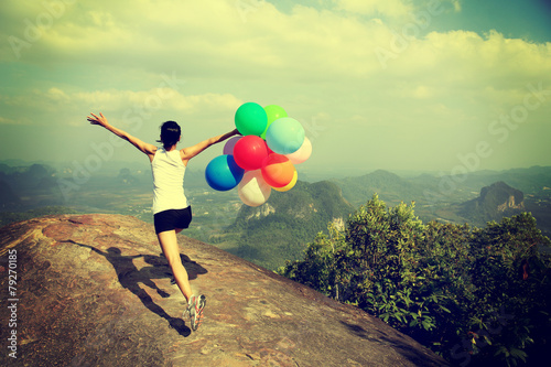 young asian woman mountain peak running with colored balloons 