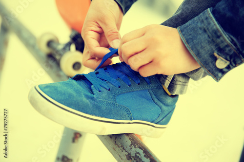 skateboarder hands tying shoelace on skatepark