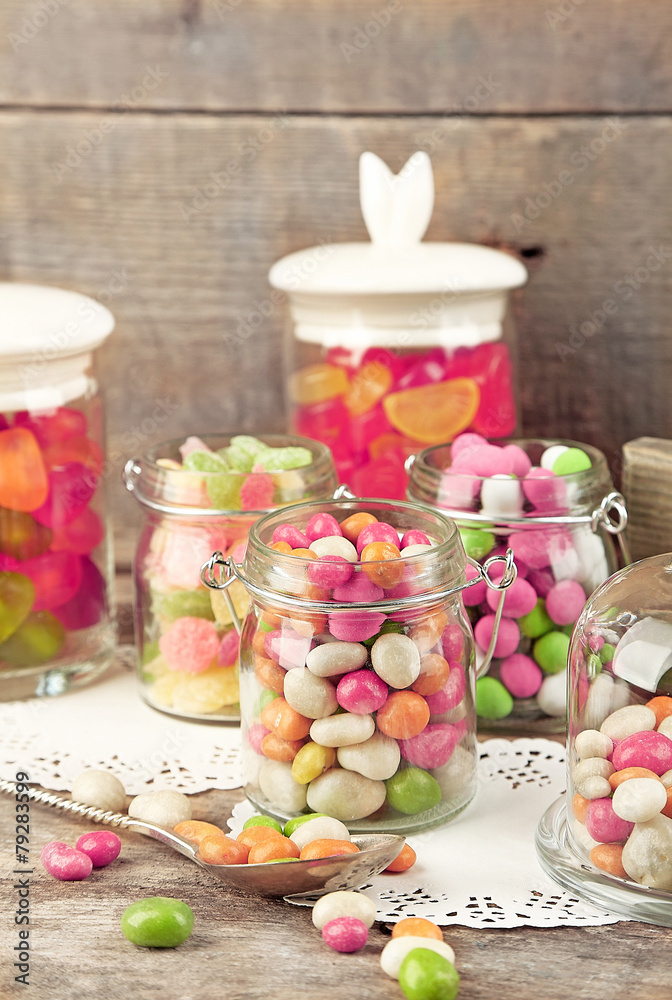 Multicolor candies in glass jars on wooden background