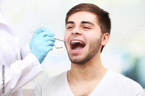 Examine of young man by dentist on light blurred background