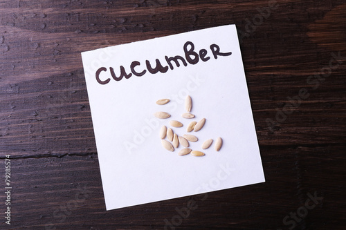 Cucumber seeds on piece of paper on wooden background