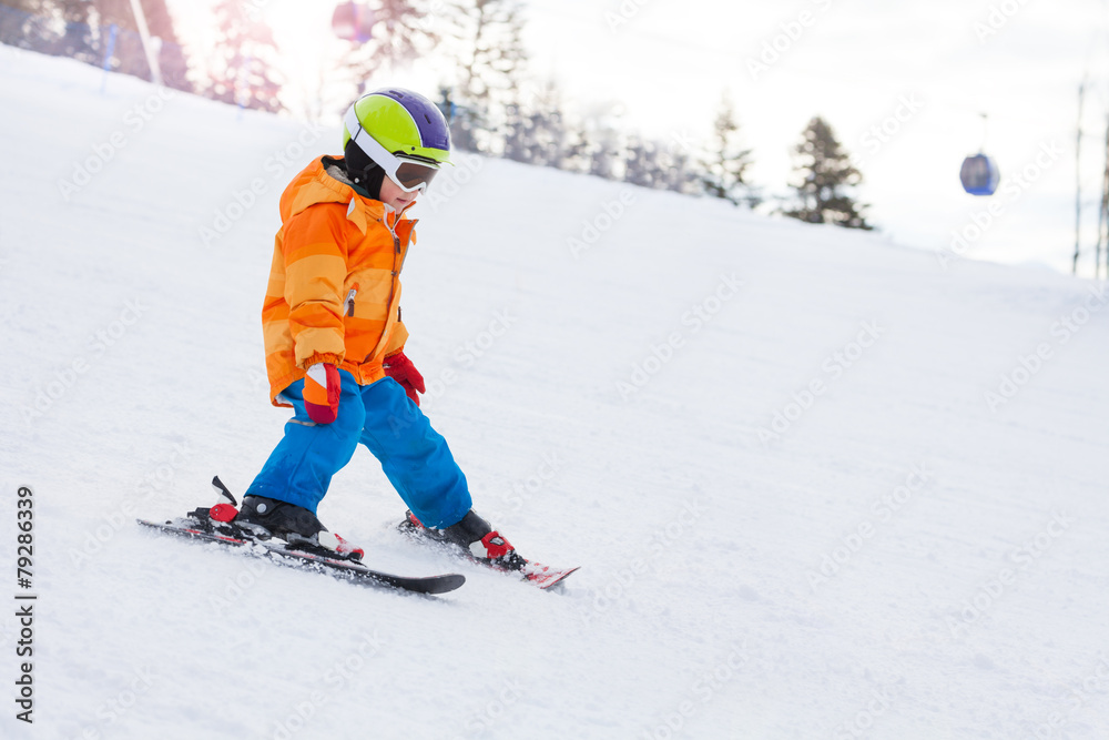 Skiing boy in ski mask, helmet on mountain slope