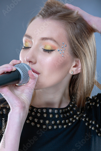 Portrait of a beautiful blonde young woman singing into micropho photo