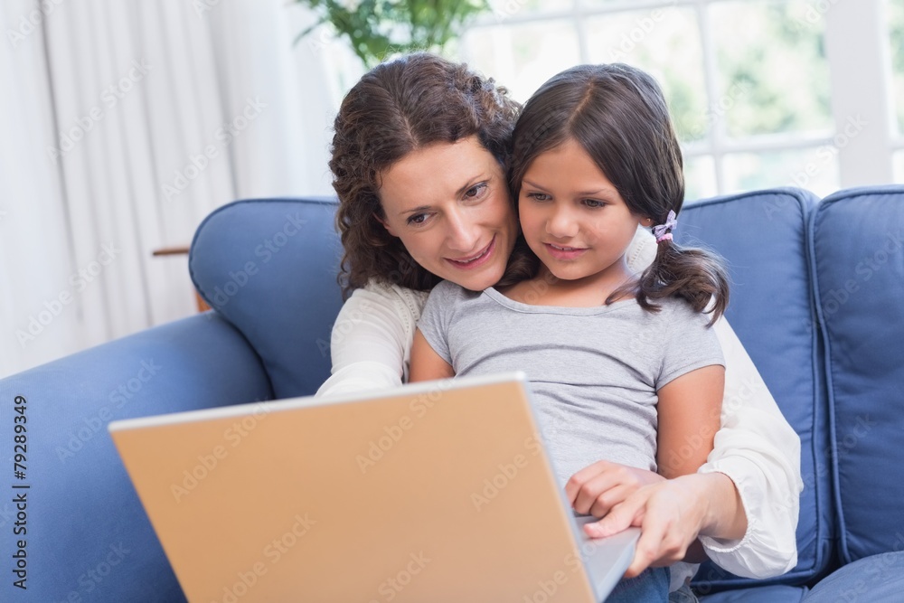 Happy mother and daughter sitting on the couch and using laptop Happy mother and daughter sitting on the couch and using laptop