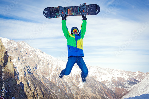 Snowboarder at jump inhigh mountains at sunny day photo