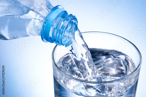 Close-up Pouring glass of water from a plastic bottle on blue ba