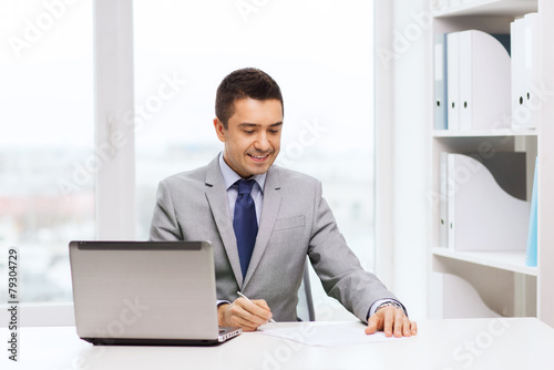 smiling businessman with laptop and papers