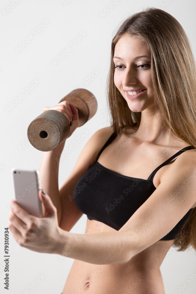 Smiling sporty girl holding dumbbell and taking selfie with smar Smiling sporty girl holding dumbbell and taking selfie with smar