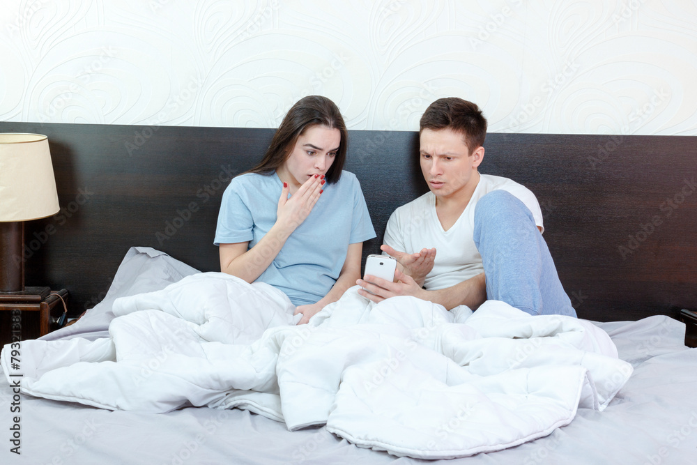 Fototapeta premium Young man looking phone with shocked and surprised woman next to