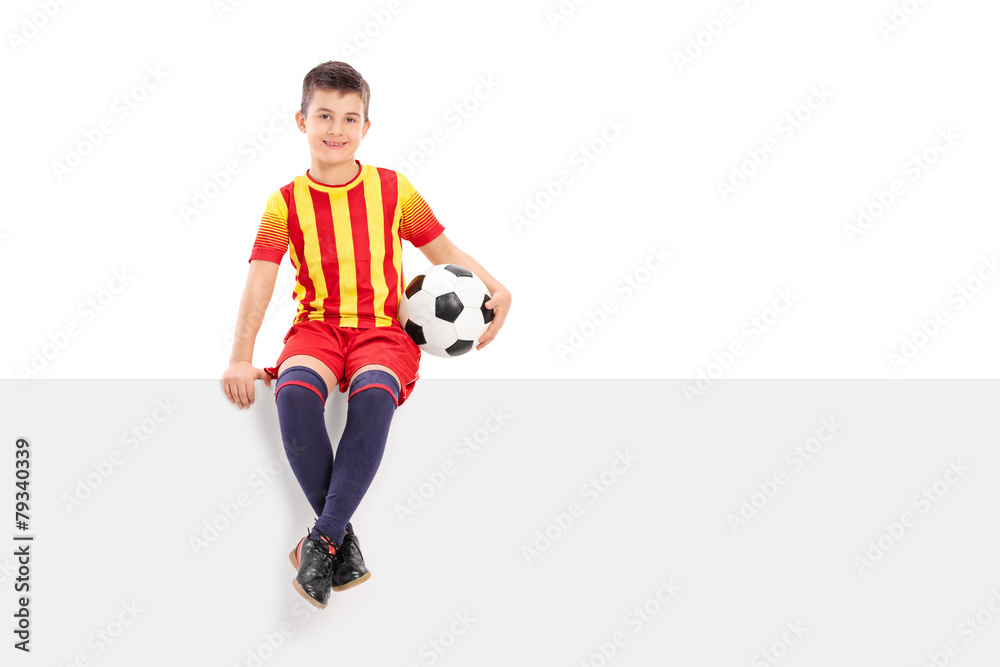 Junior soccer player sitting on a signboard