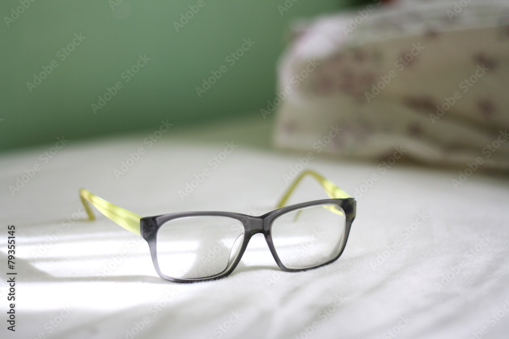Eyeglasses lying on the bed, illuminated by sunlight.