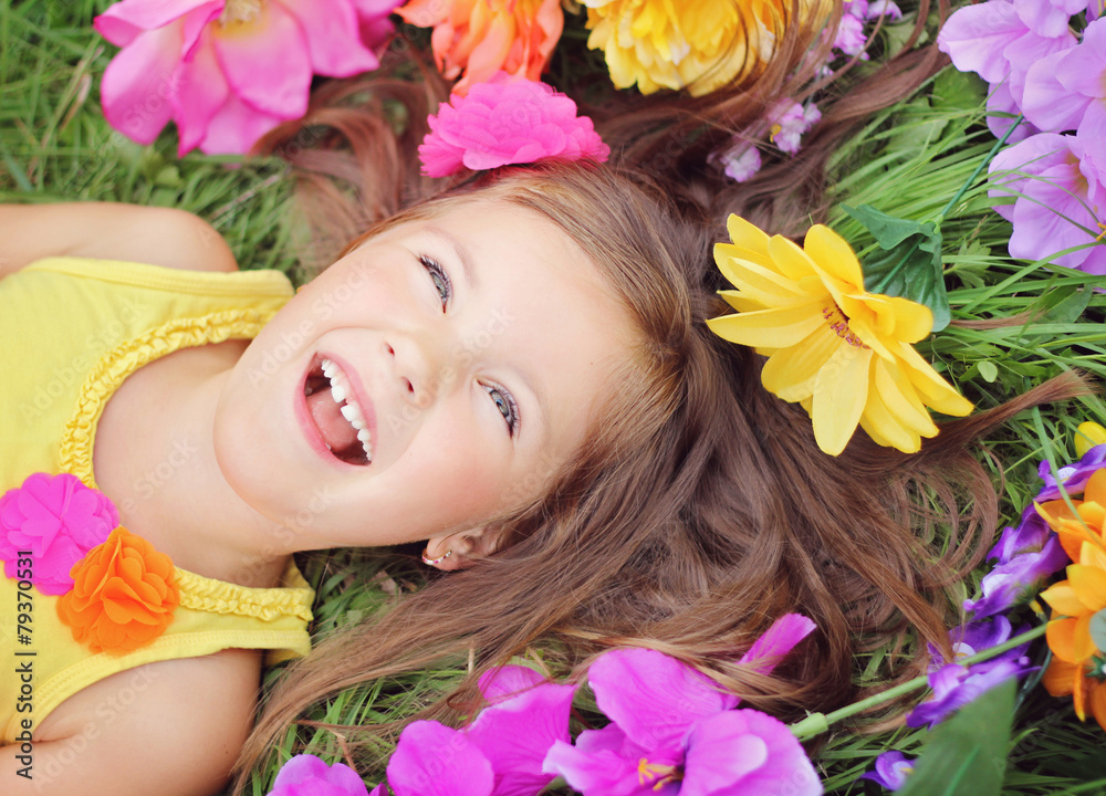 Happy little girl crown laying on the grass with flowers Happy little girl crown laying on the grass with flowers