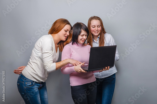 Three girls girlfriends, looking laptop on a gray background