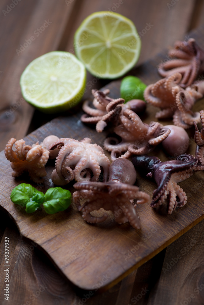 Rustic wooden cutting board with baby octopuses, studio shot Rustic wooden cutting board with baby octopuses, studio shot