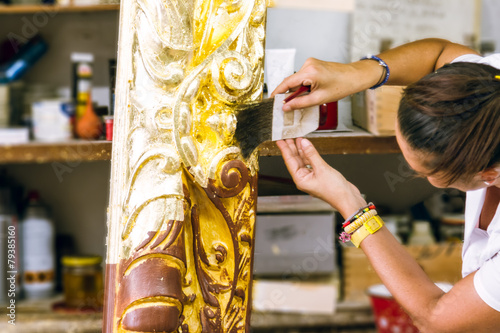 Female artisan applies golden leaf to a big wooden picture frame