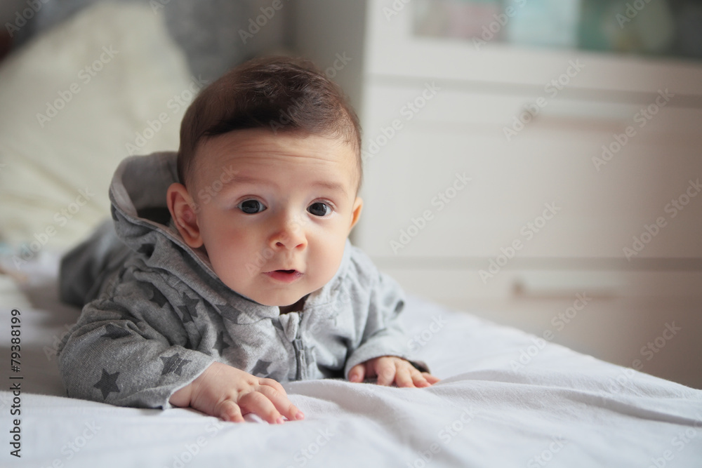 Small baby lying on the bed in white room.On his face interest a