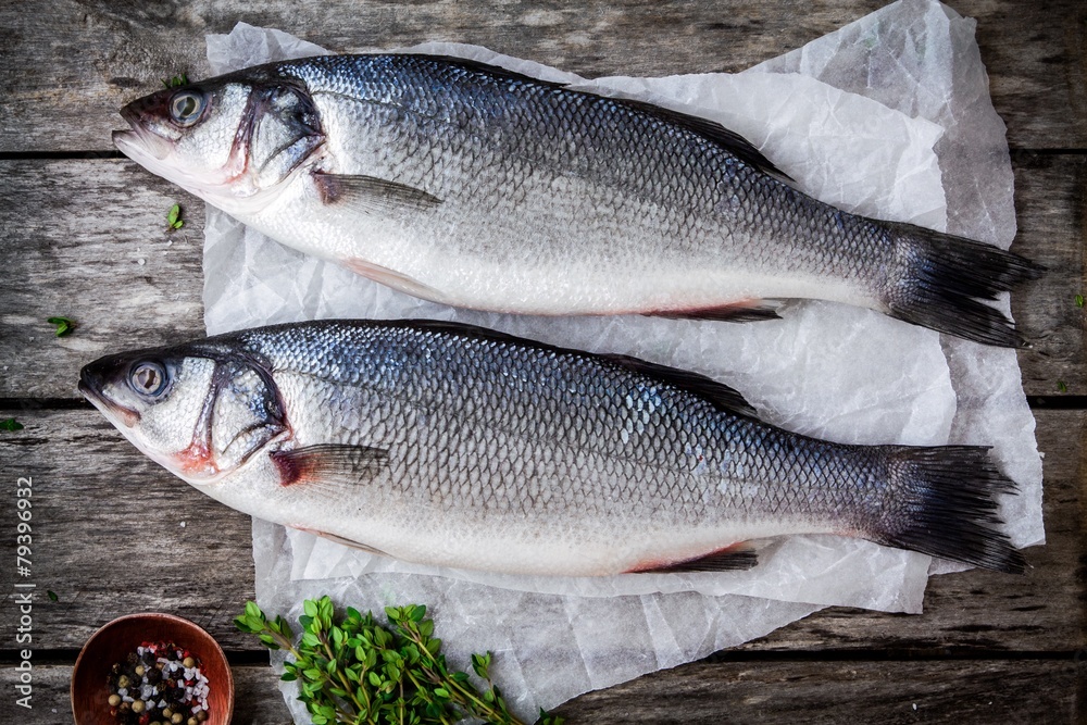 two raw seabass with fresh thyme on wooden table two raw seabass with fresh thyme on wooden table