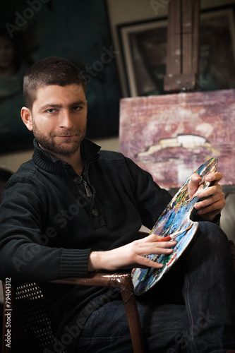 Young artist in his studio working on an oil painting.
