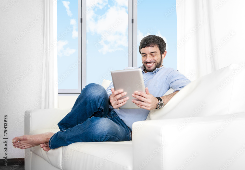 Young Hispanic man at home on couch using digital tablet Young Hispanic man at home on couch using digital tablet