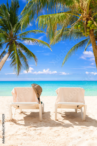 Pair of deck chairs on a tropical beach between coconut palms