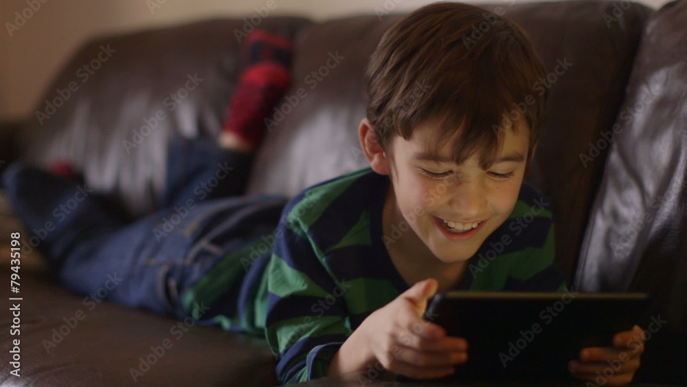 Portrait of a young boy engrossed in playing games on a touchscreen tablet