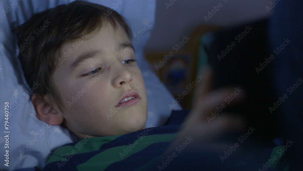 Young boy engrossed in playing games on a touchscreen tablet before bedtime