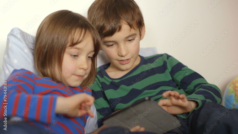 Little sister and elder brother playing games on a touchscreen tablet Little sister and elder brother playing games on a touchscreen tablet