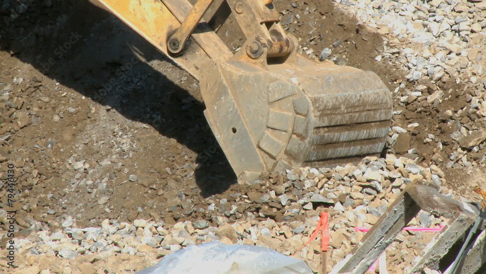 A backhoe scoops up gravel. The is a clip from a series about
