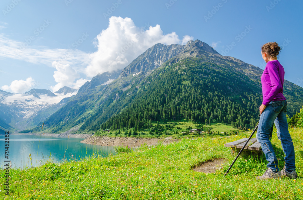 Naklejka premium A young mountaineer with poles stands beside an azure mountain