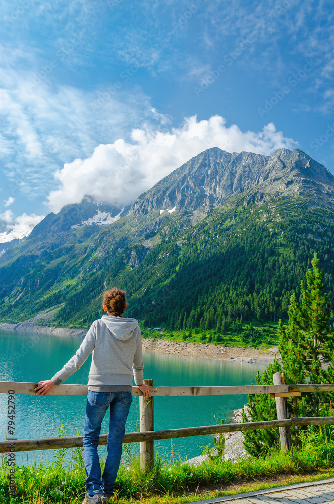A young tourist stands beside an azure mountain lake