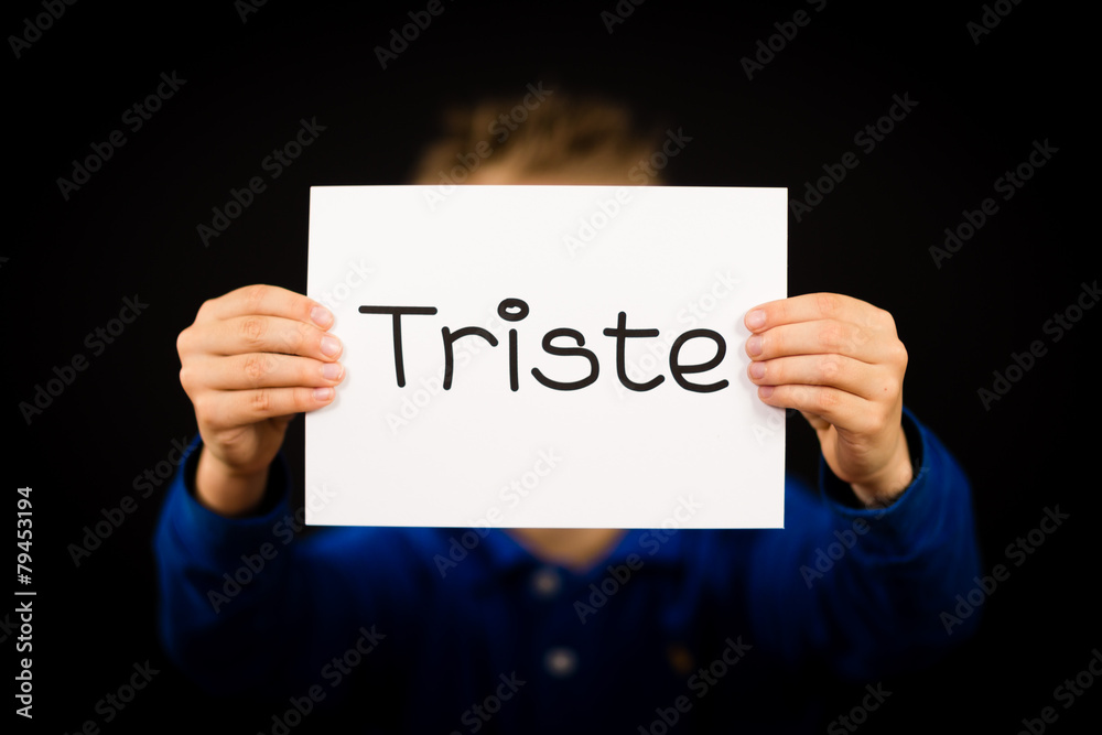 Child holding sign with Spanish word Triste - Sorry Child holding sign with Spanish word Triste - Sorry