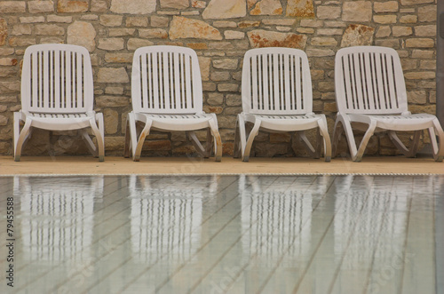 White plastic seats standing on a terrace next to a pool photo